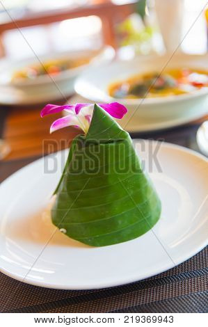 Closeup of steam rice wrapped in cone shape banana leaf with orchid flower served in Aonang Krabi Thailand