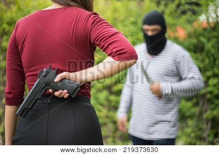 Criminal or Bandit wear black mask use knife trying to rob money from woman but she hide gun behind her concept of winner fighting usurpation.