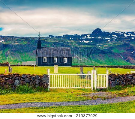 Black wooden Budakirkja church at Saefellsnes. Dramatic summer morning with field of fresh green grass on Snafellsnes peninsula western Iceland Europe. Artistic style post processed photo.