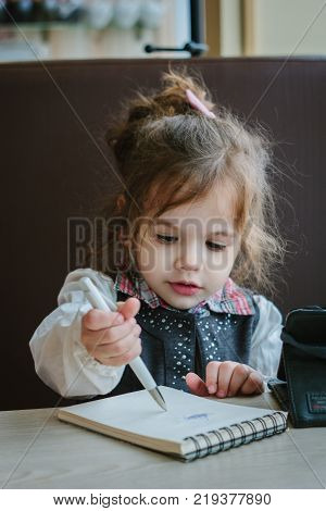 Little kid girl writing or drawing with pen in scetch book.