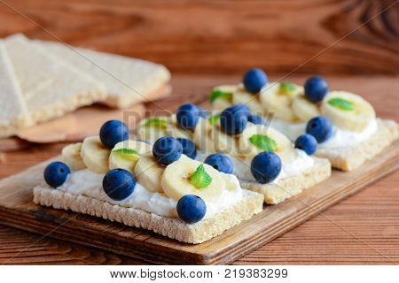Crispbreads with cottage cheese, banana and berries on wooden board. Cottage cheese open sandwich photo. Closeup