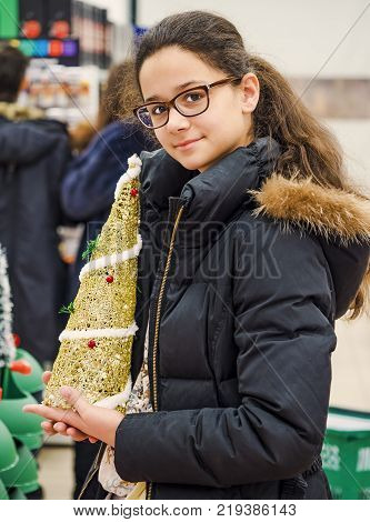 Cheerful smiling girl in glasses with diopters choosing gifts at Christmas fair