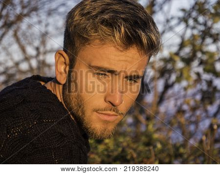Handsome young man outdoor in winter fashion, wearing black coat and woolen scarf in city park