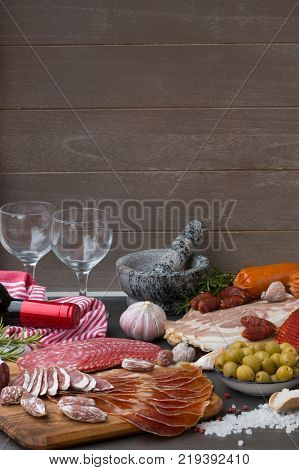 Set of different Spanish embutido, like fuet, jamon, chorizo and lomo embuchado with a red wine and two wine glasses.