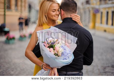 pretty blonde girl with a bouquet of flowers including roses astilba carnations and hydrange hugs her boyfriend
