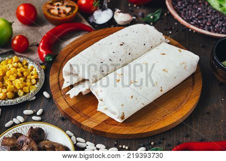 Vegetarian Burrito On Wooden Board Over Black Table Surrounded By Ingredients