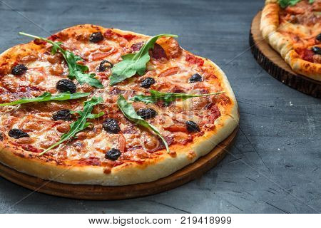 Homemade pizza with tomato, salumi, arugula and olives. Top view stone background.