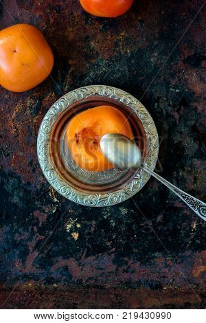 Someon start to eat persimmon on siver plate over rustic surface