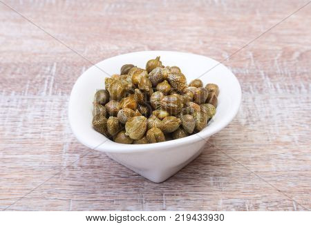 bowl with fresh capers on wooden table.