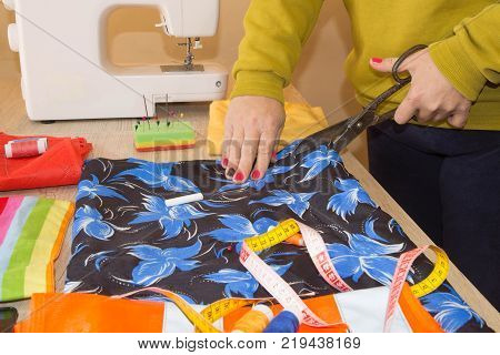 pattern scissors tape measure and a sewing machine. Workplace of seamstress. Dressmaker cuts dress detail on the sketch lines. Garment industry tailoring concept