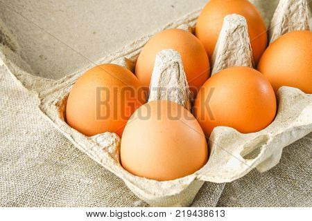 Raw brown chicken eggs in a cardboard tray with cells on sacking on a white wooden table. Ingredients for cooking
