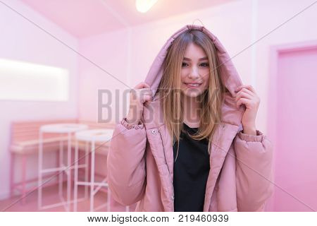 A smiling girl in a pink jacket looks at the camera and smiles at the background of the studio with pink interior. Pink life.