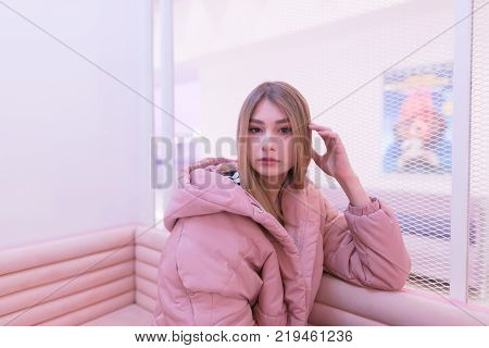 Beautiful blonde girl in pink dress poses to the camera in a pink interior. Portrait of beautiful girl in pink