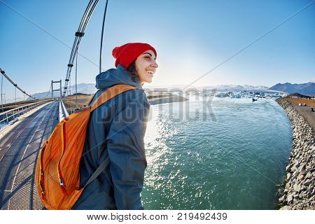 Cheerful woman wearing in red cup walks on the brige in Jokulsarlon Ice Lagoon, Iceland