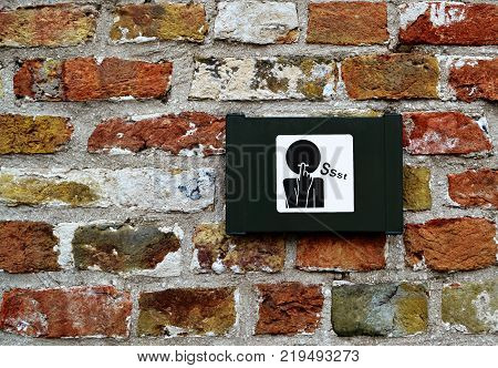 Sign/symbol of request for silence/mute on brick wall in Bruges/Brugge, Belgium.