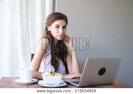 Woman having coffee and working outside. Working on laptop during her vacation in a tropical hotel. 
