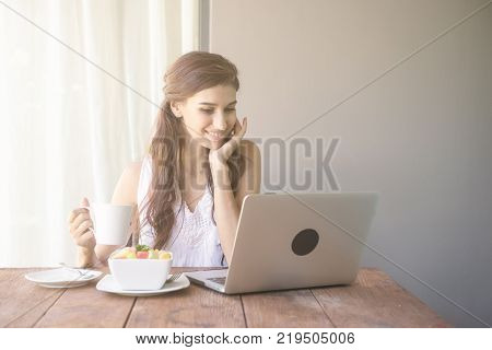 Woman having coffee and working outside. Working on laptop during her vacation in a tropical hotel. 