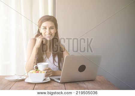 Woman having coffee and working outside. Working on laptop during her vacation in a tropical hotel. 