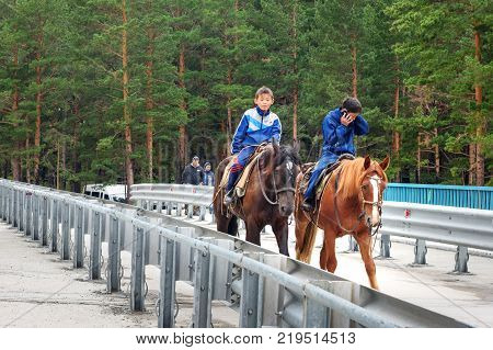 Arshan Russia - August 15 2017: Two Buryat boys ride horses on bridge over the Kyngyrga River. Buryatia