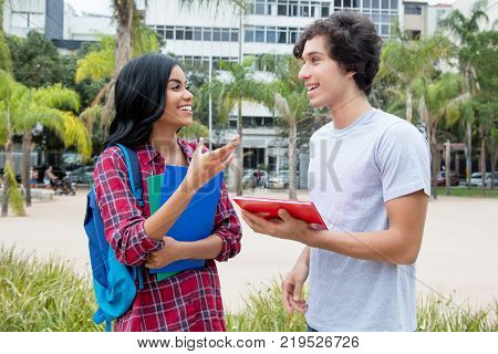 Native latin american female student talking with caucasian friend outdoors on campus of the university