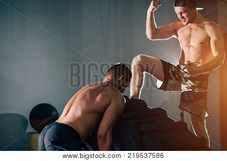trainer standing on tire and scream at a man exercising with a tire