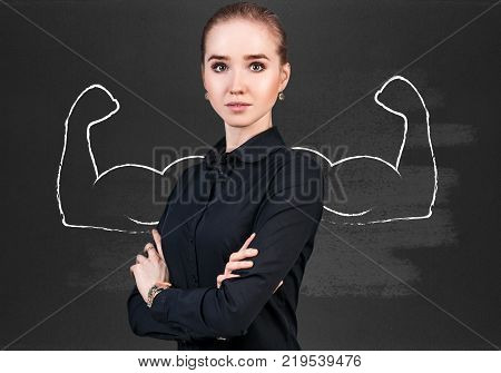 Business woman stands over chalkboard with drawn powerful hands.