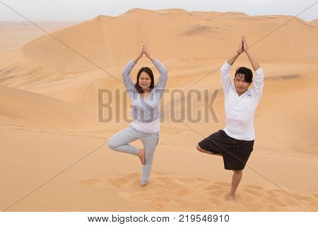 An Indonesian girl and Filipino boy doing a yoga tree on Dune 7, the highest sand dune in the world, in Walvis Bay, Namibia