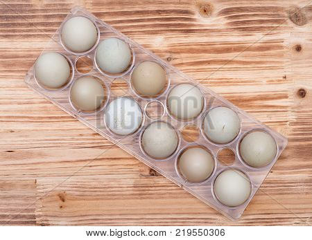 Unwashed fresh organic gmo and soy free pasture raised chicken eggs in clear plastic container on wooden vintage background