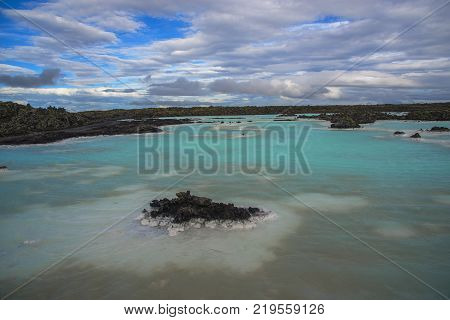 Geothermal (with mineral) blue lake and black lava stones. Beaitiful sky in background.
