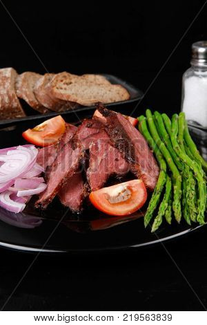 business lunch fresh roast beef meat slices on black plate wotj cutlery asparagus boiled broccoli rye bun on wooden table