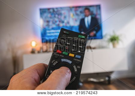 POV-Shot from a young man holding a TV Remote control to chance the tv channel on 4k TV at home. ideal for websites and magazines layouts