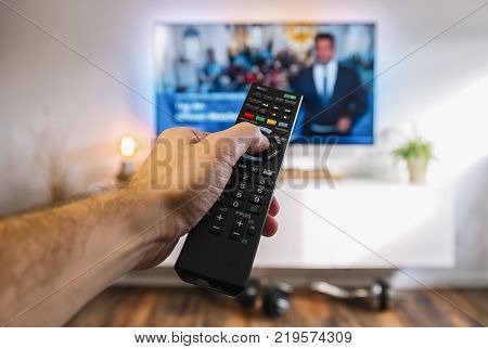 POV-Shot from a mans hand holding a TV Remote control to ZAP on tv at home. ideal for websites and magazines layouts