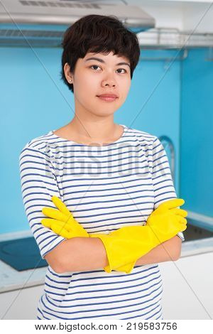 Confident Asian female cleaner looking at camera and ready to make kitchen tidy. Serious attractive housewife in rubber gloves crossing arms on chest. Housekeeping concept