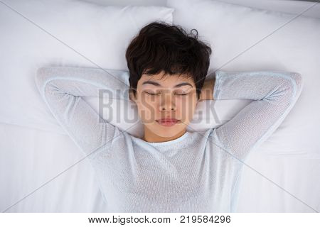 Peaceful Asian woman relaxing in bed enjoying calmness. Serene young woman with short hair sleeping alone or meditating on bed. Tranquility concept