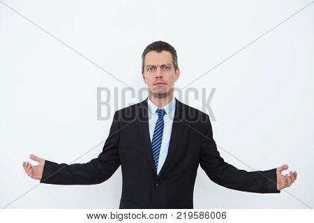 Portrait of serious young Caucasian businessman wearing suit standing and outstretching arms. Confusion and do not know concept