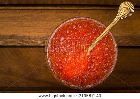 Red caviar in glass jar with gold spoon close up. Sea food. Healthy eating. Diet. Wooden rustic background. Top view. Selective focus