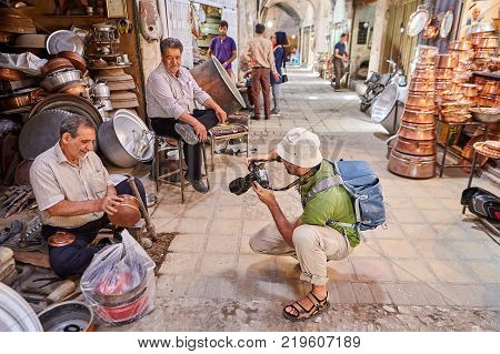 Yazd Iran - April 22 2017: Tourist takes pictures of Iranian man at work old coppersmith produces copper pot in his workshop in bazaar.