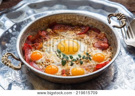 Fried egg and cured meat in copper pan, close view.