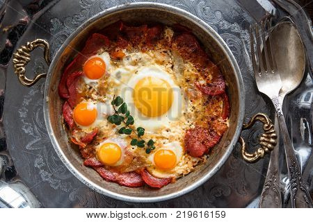 Closeup of Turkish pastirmali and fried egg in a copper pan on wooden table.