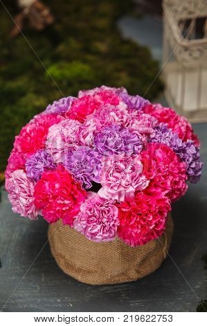 bouquet of carnations in a basket from a fabric of flax. Colorful bouquet at table.