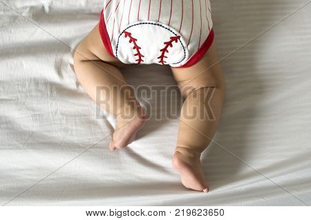 A baby in prone position is wearing a red and white striped baseball clothing