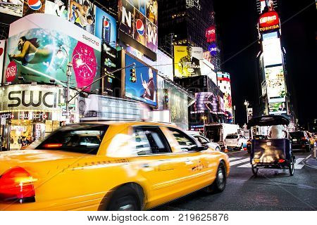 Times Square, New York City, New York, United States - circa 2014 - taxi cab driving in motion blurry times square night new york city with play marquees and brightly lit advertising signs and lots of people