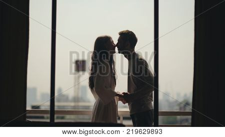 Young happy couple kissing and enjoying the view from a balcony overlooking city in morning during their honeymoon