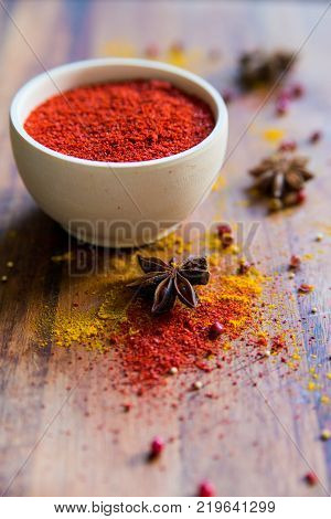 Close up white wooden bowl filled with paprika powder on dark wooden surface covered with anise and turmeric