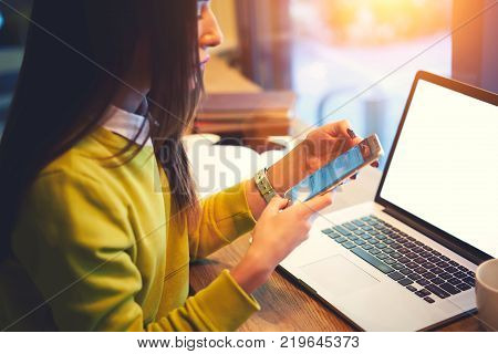 Cropped image of young hipster girl reading notification on smartphone while working on freelance