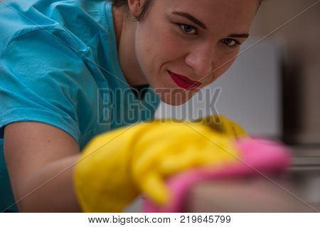 Portrait of beautiful young woman co-worker of cleaning company wipes furniture with rag in rubber gloves on her hands