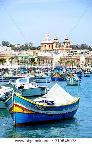 MARSAXLOKK, MALTA - APRIL 1, 2017 - Traditional Maltese Dghajsa fishing boats in the harbour with the parish church of Our Lady of Pompei to the rear Marsaxlokk Malta Europe, April 1, 2017.