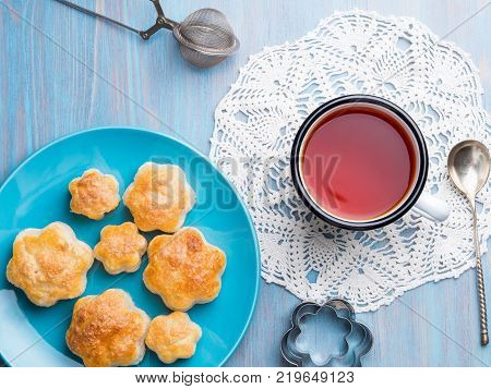 traditional breakfast with a cup of tea and sweet pastries. A plate of scones a mug of tea spoon tea strainer napkin on a wooden blue table top view rustic style.