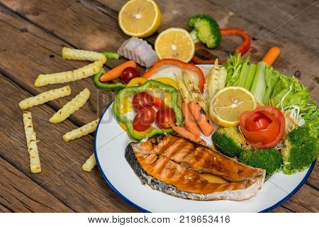 Salmon steak Grilled salmon on an old wooden table with fried taro, sweet chilli, carrots and other side dishes on the table.
