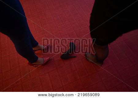 Close up feet of women's feet on dark red floor one took off her shoe because she feels tired